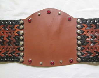 May include: A brown leather belt with a woven design and silver studs. The belt has red gemstones on the front.