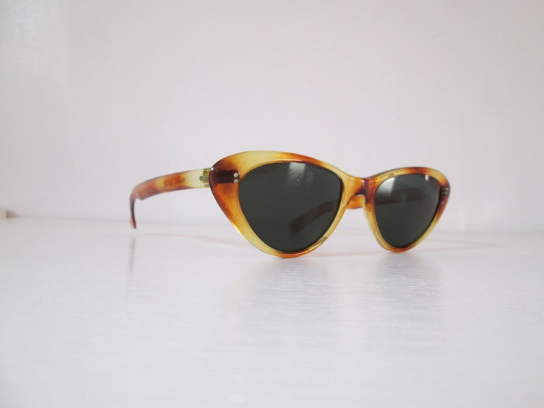 Puede incluir: Gafas de sol de ojo de gato con un patr&oacute;n de carey. Las monturas presentan tonos &aacute;mbar y marr&oacute;n, con lentes oscuras. Estas gafas tienen una est&eacute;tica retro y vintage.