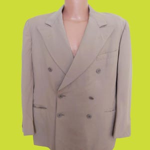 May include: A double-breasted blazer in a light beige color. The blazer has four buttons down the front and two pockets on the sides.