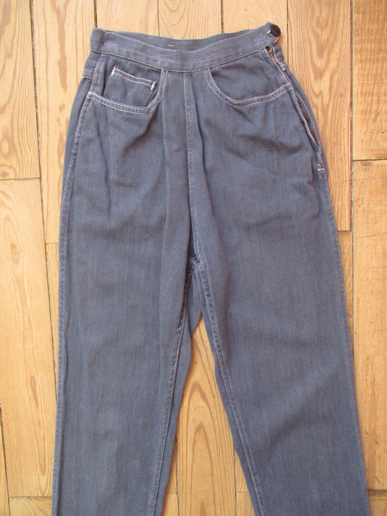May include: A pair of blue denim pants with a high waist and a button closure. The pants have front pockets with white stitching and a zipper on the side. The pants are made of a durable denim material.