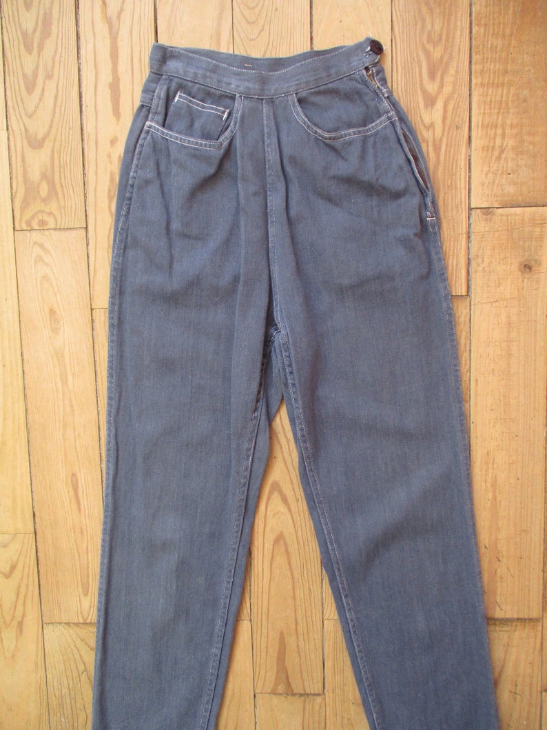 May include: A pair of gray denim pants with a high waist and straight leg. The pants have front pockets with white stitching and a button closure. The fabric appears to be a medium weight denim.