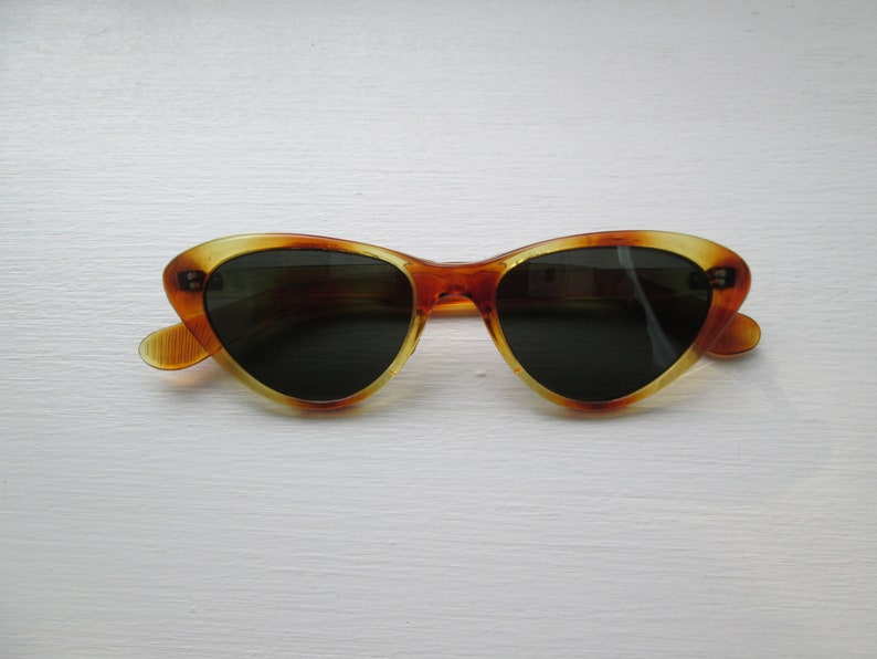 Puede incluir: Gafas de sol de ojo de gato con un patr&oacute;n de carey. Las monturas son &aacute;mbar y marr&oacute;n, con lentes oscuras. Las gafas de sol tienen un dise&ntilde;o retro cl&aacute;sico.