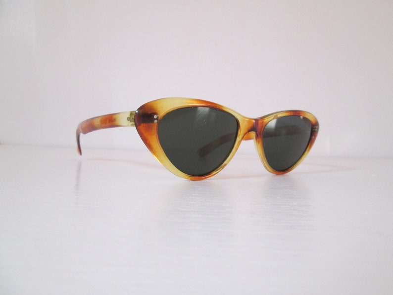 Puede incluir: Gafas de sol vintage de ojo de gato con estampado de carey. Las monturas son una mezcla de tonos &aacute;mbar y marr&oacute;n, con lentes oscuras. Dise&ntilde;o retro cl&aacute;sico.