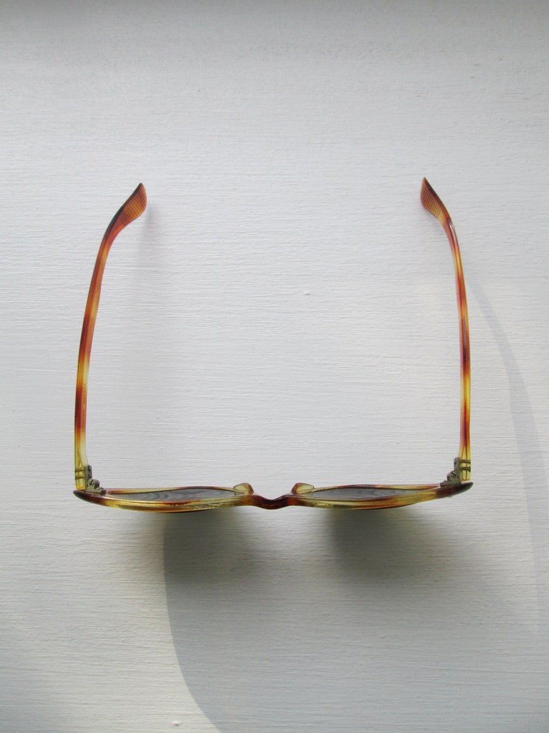 Puede incluir: Gafas con estampado de carey y lentes oscuras. Las monturas presentan una paleta de colores c&aacute;lidos en &aacute;mbar, marr&oacute;n y amarillo. Las gafas est&aacute;n sobre un fondo blanco, con una sombra proyectada a un lado.