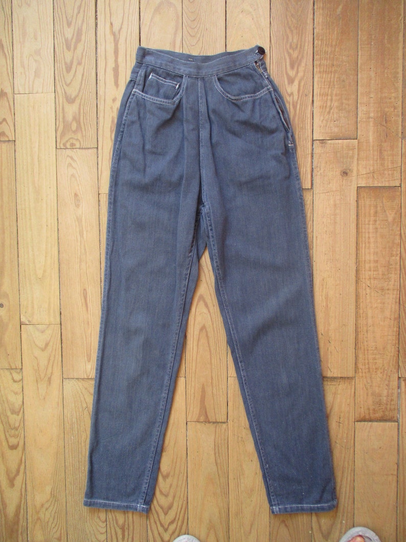May include: A pair of high-waisted, dark blue denim pants. The pants have a button closure, front pockets, and a straight leg design. The denim appears to be a medium weight, suitable for various seasons.