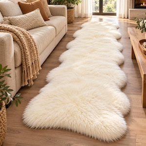 May include: A long, off-white sheepskin runner rug featuring a thick, plush, and shaggy texture. The rug is composed of multiple connected pelt shapes, creating an elongated, organic silhouette that extends across the floor surface.