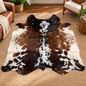 May include: A cowhide rug featuring a natural, irregular shape with a tri-color pattern of dark brown, black, and white patches. The hide displays a dense, mottled distribution of colors across its surface, creating a distinct, organic appearance.