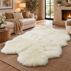 May include: A large, off-white faux sheepskin rug with a thick, plush, and shaggy texture. The rug features an irregular, organic shape with soft, rounded edges, designed to lay flat on a floor surface, providing a dense and soft pile appearance.