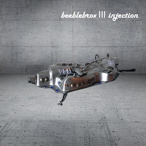 May include: A metallic, silver-toned sculpture with an elongated, aerodynamic form featuring the text 'beeblebrox ||| injection' at the top. The object displays 'DSA' labels, small blue circular accents, and thin wire components, supported by a single thin leg.