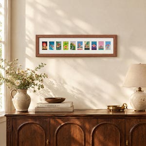 Puede incluir: Un marco de pared rectangular horizontal que presenta diez pequeñas ilustraciones coloridas dispuestas en fila sobre un paspartú blanco. El marco tiene un acabado de madera marrón texturizada y contiene varias escenas con personajes.