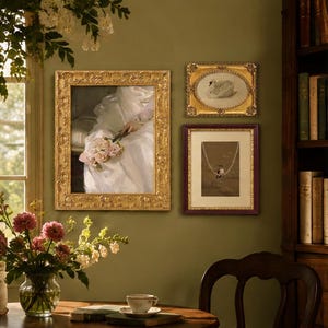 Puede incluir: Tres cuadros de pared enmarcados: un marco dorado rectangular vertical grande con una pintura de una persona sosteniendo flores rosas, un marco dorado ovalado horizontal pequeño con una ilustración de un cisne y un marco rectangular con un ave.