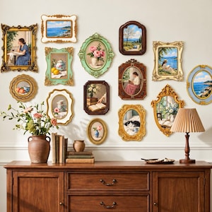 Puede incluir: Una pared de galería con doce marcos decorativos de diversas formas y colores, incluyendo oro, verde y marrón. Los marcos contienen pinturas de paisajes, bodegones y figuras. Un aparador de madera se encuentra debajo.