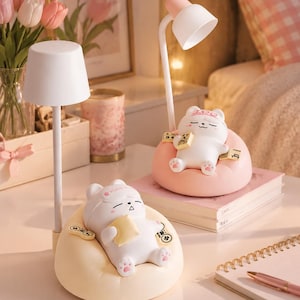 May include: Two desk lamps featuring white, rounded shades on thin poles. Each base is a soft, beanbag-style chair holding a white cartoon bear figure. One bear sits in a pink chair with mahjong tiles, while the other sits in a cream chair holding a pillow.