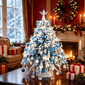 Könnte beinhalten: Ein Tisch-Weihnachtsbaum mit blau-weiß beflockten Zweigen, beleuchtet durch eine Lichterkette. Er ist mit blau-weißen Kugeln, Schneeflocken, einer kleinen Hirschfigur und einem transparenten Engel als Baumspitze auf einem weißen Sockel geschmückt.