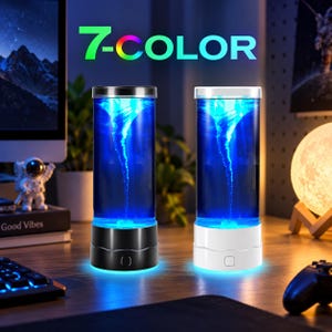 Könnte beinhalten: Zwei zylindrische Tornadolampen mit blauem Flüssigkeitswirbeleffekt. Eine Lampe hat einen schwarzen Sockel, die andere einen weißen. Beide haben einen klaren Glaskörper und einen quadratischen Einschaltknopf. Der Text 7-COLOR ist zu sehen.