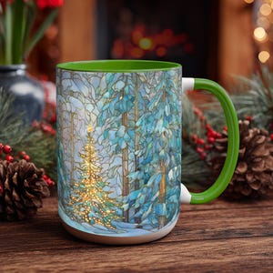May include: A ceramic mug with a green handle and interior, featuring a wrap-around stained glass style illustration of a glowing Christmas tree in a snowy forest. The design displays blue and white winter trees with a bright, illuminated tree.