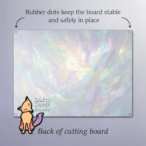 May include: A rectangular glass cutting board with a floral design in pastel colors. The back of the board has rubber dots for stability. The text "Crafty Coyote Studio" and "Back of cutting board" are visible.