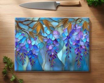 May include: A rectangular glass chopping board featuring a stained glass style illustration of hanging wisteria flowers in shades of blue and purple with golden brown leaves, positioned below a stainless steel kitchen knife with a wooden handle.