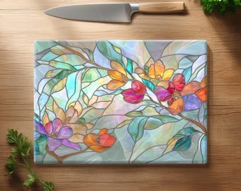 May include: A rectangular glass chopping board featuring a colourful stained glass pattern of blooming flowers and leaves in shades of red, orange, yellow, purple, and teal, positioned below a stainless steel kitchen knife with a wooden handle.