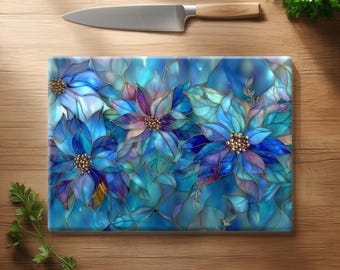 May include: A rectangular glass cutting board with a floral design featuring blue and purple poinsettias with gold accents. A stainless steel knife with a wooden handle rests above the board on a wooden surface.