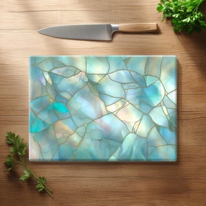 Può includere: Un tagliere rettangolare caratterizzato da un motivo marmorizzato azzurro e bianco con sottili venature color oro che ricordano la pietra incrinata. Un coltello da chef in acciaio inossidabile con manico in legno chiaro è posizionato orizzontalmente.