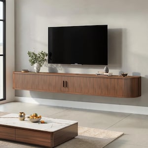 May include: A wall-mounted brown wooden media console with a vertical slatted front and rounded edges, featuring two cabinet doors with thin vertical handles. A flat-screen television is mounted on the wall directly above the console unit.
