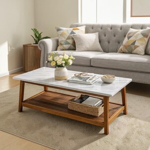 May include: A rectangular coffee table with a white faux marble top and a dark wood frame featuring a lower shelf. The table holds a ceramic vase with white flowers, a stack of magazines, a pair of glasses, and a small bowl of beads.