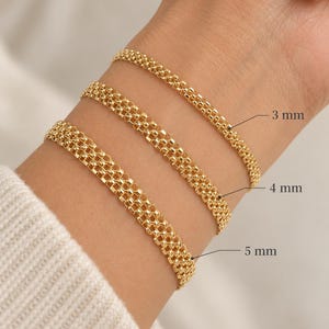 Puede incluir: Tres pulseras de cadena en tono dorado con una textura tejida similar a una malla. Las pulseras están etiquetadas con anchos de 3 mm, 4 mm y 5 mm, lo que indica el grosor variable de cada pieza individual en este conjunto de joyería.