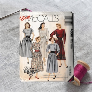 May include: A McCall's sewing pattern envelope labeled 4558 featuring illustrations of four different dress styles. The cover displays text including Fashion Basics and McCall's, with a barcode on the right side and a needle and thread nearby.