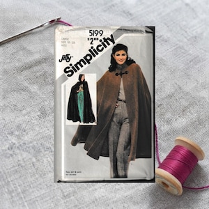 May include: A Simplicity 5199 sewing pattern envelope for a cape, featuring a brown cape with a toggle closure and a smaller inset image of a black cape. The text includes Simplicity, 5199, Jiffy, and size 18-20 large, with a price of $2.00.