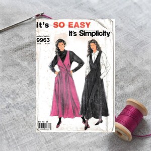May include: A Simplicity sewing pattern envelope 9963 featuring illustrations of two sleeveless dresses worn over long-sleeved tops. The text reads It's SO EASY it's Simplicity. The pattern is for sizes 8-20. A spool of magenta thread and a needle are visible.