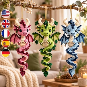 May include: Three crocheted dragon ornaments hanging from a branch. Each dragon features a cream-colored belly, large dark eyes, horns, and wings. One dragon is pink with dark pink accents, one is green with dark green accents, and one is blue.