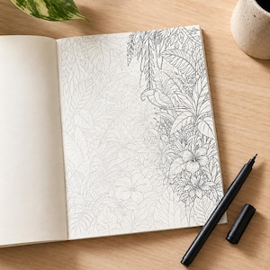 May include: An open colouring book featuring a detailed black and white line drawing of a tropical jungle scene with various leaves, flowers, and a toucan perched on a branch. A black felt-tip pen with its cap removed lies next to the open notebook.