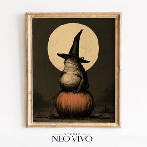May include: A framed wall art print featuring a toad wearing a black pointed witch hat, sitting atop a large orange pumpkin. Behind the toad is a large, pale yellow full moon set against a dark, muted background. The frame is light brown wood.