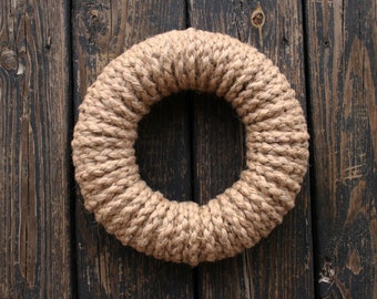 May include: A brown rope wreath, made of thick, twisted rope, against a dark wood background.