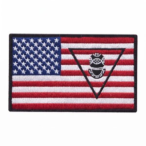 Puede incluir: Un parche rectangular bordado que muestra la bandera de los Estados Unidos con franjas horizontales rojas y blancas y un cantón azul con estrellas blancas. Un triángulo negro está centrado a la derecha, con un icono de casco de buzo.