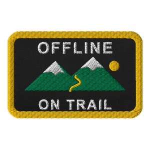 May include: A rectangular embroidered patch with a black background and a yellow border. It features two green mountains with white snow-capped peaks, a yellow sun, and a yellow winding trail. The white text reads OFFLINE ON TRAIL.