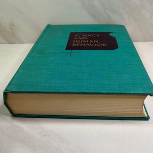 May include: A hardcover book titled Science and Human Behavior with a textured teal green cover. The front cover features a dark brown rectangular graphic with gold lettering and thin black lines. The pages are visible along the side.