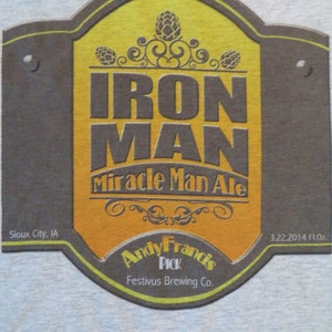 May include: A brown and yellow beer coaster with the text "IRON MAN Miracle Man Ale" and "Andy Francis PICK Festivus Brewing Co.". The coaster also includes the text "Sioux City, IA" and "3.22.2014 fl.oz."
