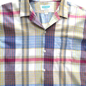 Puede incluir: Una camisa de botones a cuadros con fondo blanco y rayas rojas, azules, amarillas y marrones. La camisa tiene cuello y un bolsillo en el lado izquierdo. La etiqueta de la camisa dice "Sea Isle by Arrow".