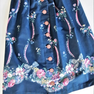Puede incluir: Una falda azul marino con estampado floral y cierre de botones en la parte delantera. La falda tiene una cintura fruncida y una longitud midi.