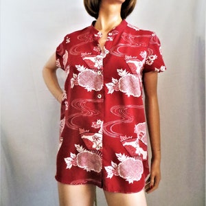May include: A red short-sleeved button-up shirt with a white floral and wave pattern.