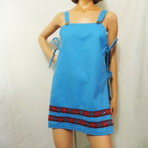 May include: A light blue mini dress with a square neckline and thin straps. The dress has a decorative trim around the hem with red, blue, and black accents. The trim features small, round, iridescent sequins.