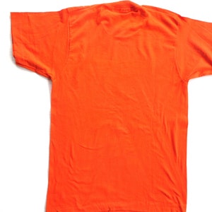 Puede incluir: Una camiseta lisa de color naranja con mangas cortas.