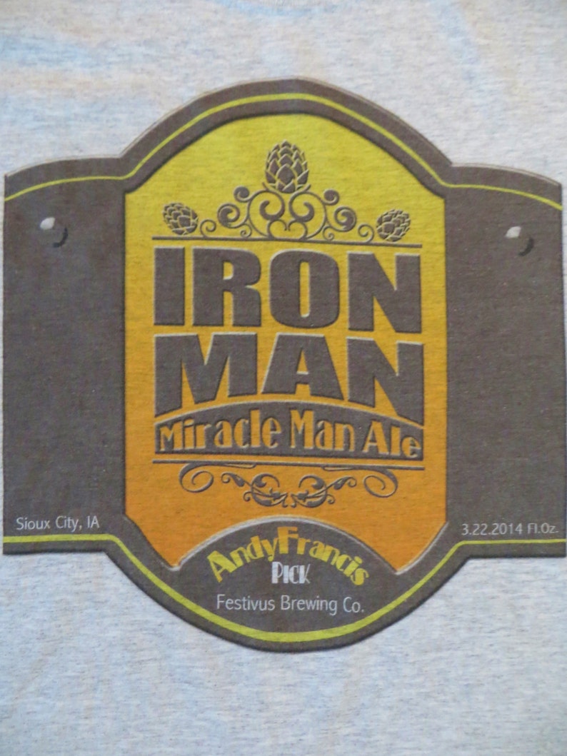 May include: A brown and yellow beer coaster with the text "IRON MAN Miracle Man Ale" and "Andy Francis PICK Festivus Brewing Co.". The coaster also includes the text "Sioux City, IA" and "3.22.2014 fl.oz."