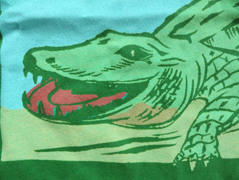 May include: Green alligator with a red open mouth and green scales on a green and blue background.