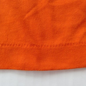 Puede incluir: Primer plano del dobladillo de tela naranja de una prenda, mostrando el detalle de la costura.