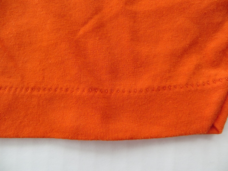 Puede incluir: Primer plano del dobladillo de tela naranja de una prenda, mostrando el detalle de la costura.