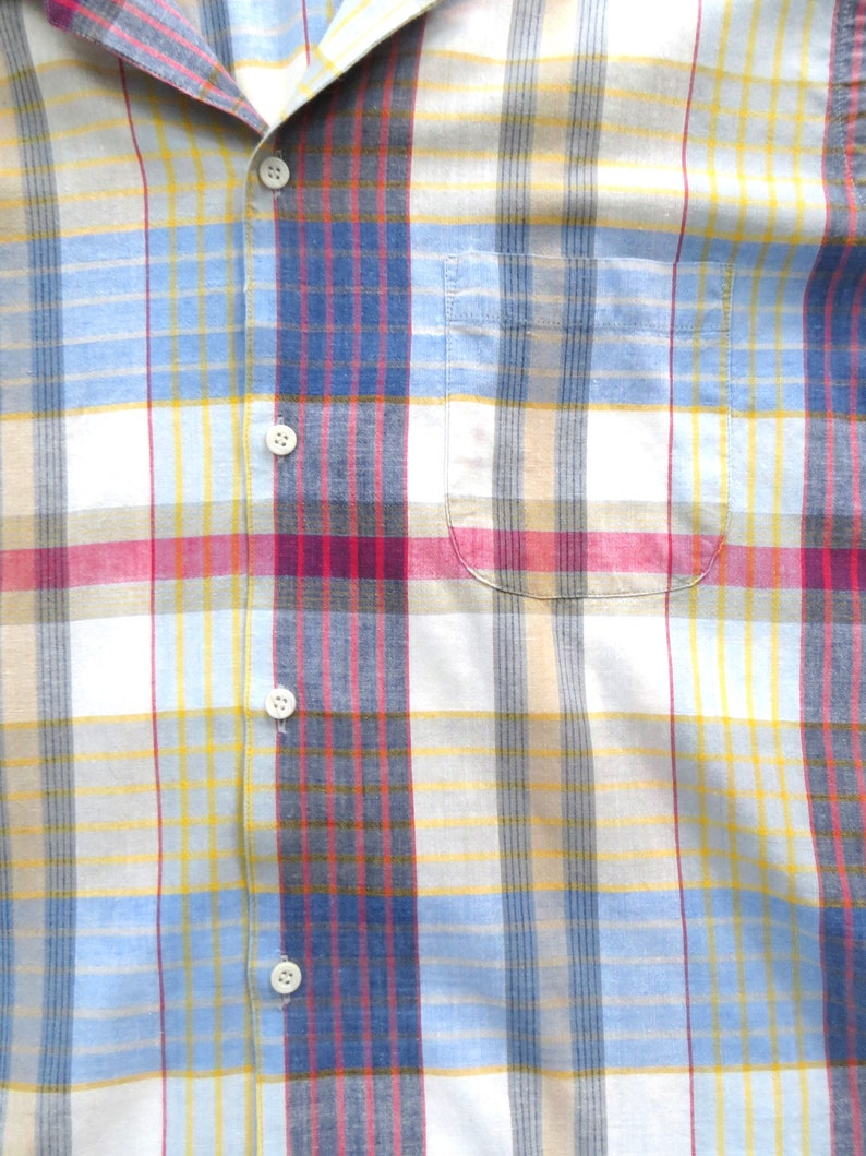 May include: A white, blue, yellow, and red plaid button-up shirt with a pocket on the left side.