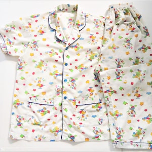 May include: White pajamas with a short-sleeved top and long pants. The pajamas feature a repeating pattern of Donald Duck with the text "Donald Duck" and "Pleuod" in a colorful design.